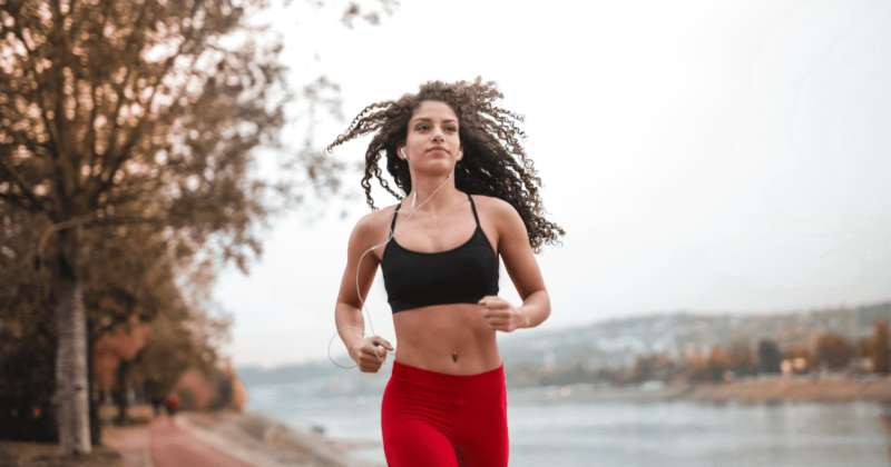 Curly woman in black top and red leggings running outdoors, curly hair