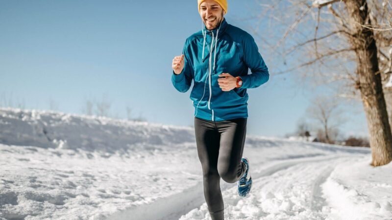man running in snow with blue vest and black joggings